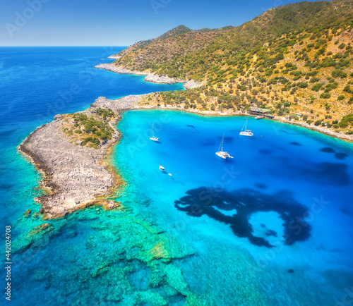 Fototapeta Naklejka Na Ścianę i Meble -  Aerial view of beautiful yachts and boats on the sea at sunset in summer. Akvaryum koyu in Turkey. Top view of luxury yachts, sailboats, clear blue water, rock, sky, mountain and green trees. Travel