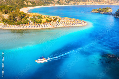 Speed boat on blue sea at sunrise in summer. Aerial view of motorboat in Blue Lagoon, sandy beach, sun beds, clear azure water. Tropical landscape with yacht, green forest. Top view. Oludeniz, Turkey