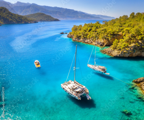 Fototapeta Naklejka Na Ścianę i Meble -  Aerial view of beautiful yachts and boats on the sea at sunset in summer in Turkey. Top view of luxury yachts, sailboats, clear blue water, rock, sky, mountain and green trees. Travel. Landscape