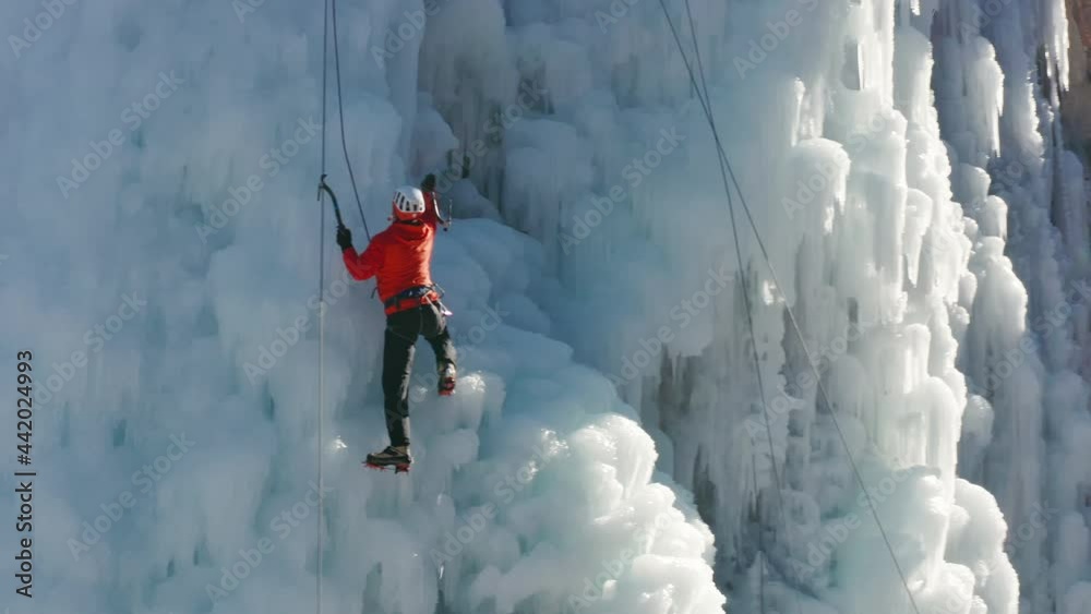 Aerial view of a frozen waterfall and rocks with climber ascending its ice-covered surface, using ice axes and crampons
