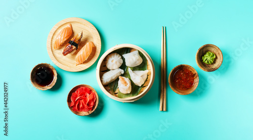 Top view of nigiri sushi set Traditional chinese steamed set dumplings Dim Sumsin bamboo steamer with soy, chilli sauces, ginger, wasabi, chopsticks on blue turquoise surf.ace. Wide long banner  photo