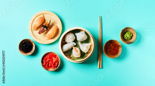 Top view of nigiri sushi set Traditional chinese steamed set dumplings Dim Sumsin bamboo steamer with soy, chilli sauces, ginger, wasabi, chopsticks on blue turquoise surf.ace. Wide long banner 