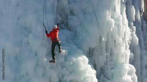 Aerial view of a frozen waterfall and rocks with climber ascending its ice-covered surface, using ice axes and crampons