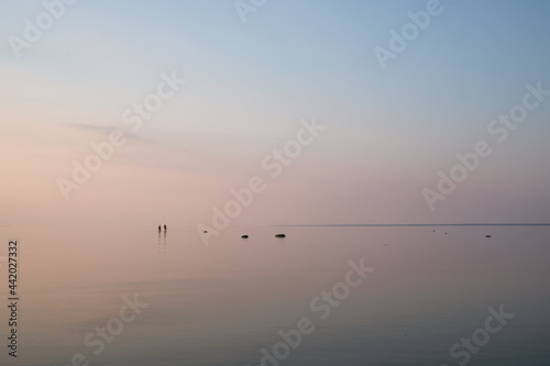 Amazing sunset with pink and blue pastel colors over the sea. Sea and sky blend together. Silhouettes of two people walking. Summer sunset at the Baltic sea, Europe. Tropical night.