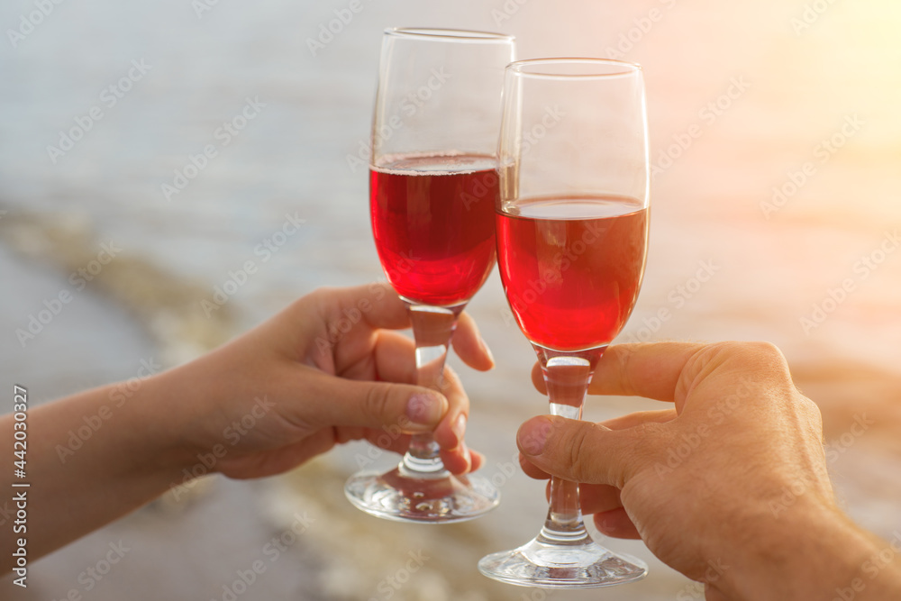 Two red wine glasses in couple hands silhouettes against sea sunset.