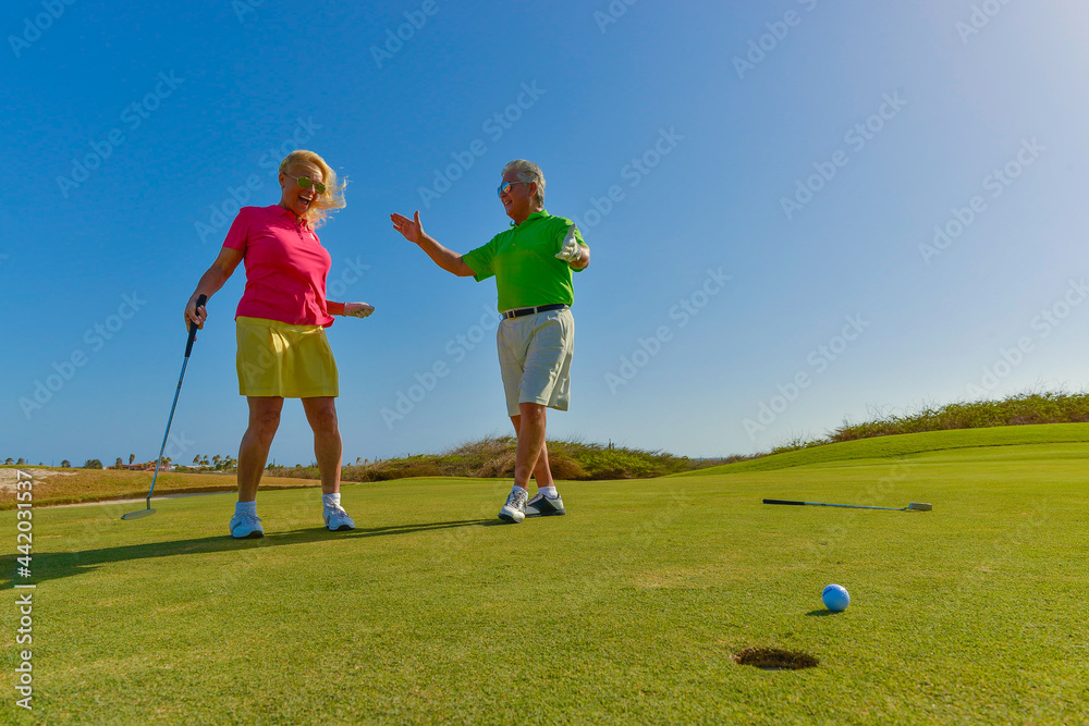 Active senior couple playing golf at sunset on the putting green.