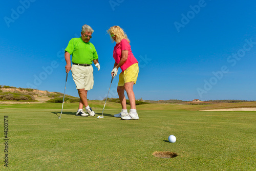 Active senior couple playing golf at sunset on the putting green.