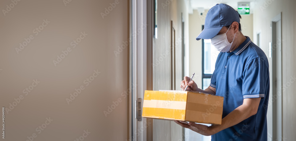 Delivery man with face mask in blue uniform holding parcel for customer, Delivery during the Covid-19 pandemic Concept Delivery man with face mask in blue uniform holding parcel for customer, Delivery during the Covid-19 pandemic Concept