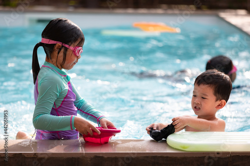Asian sibling girl and boy playing water with toy together in the swimming pool with fun. Summer activity and childhood lifestyle concept.