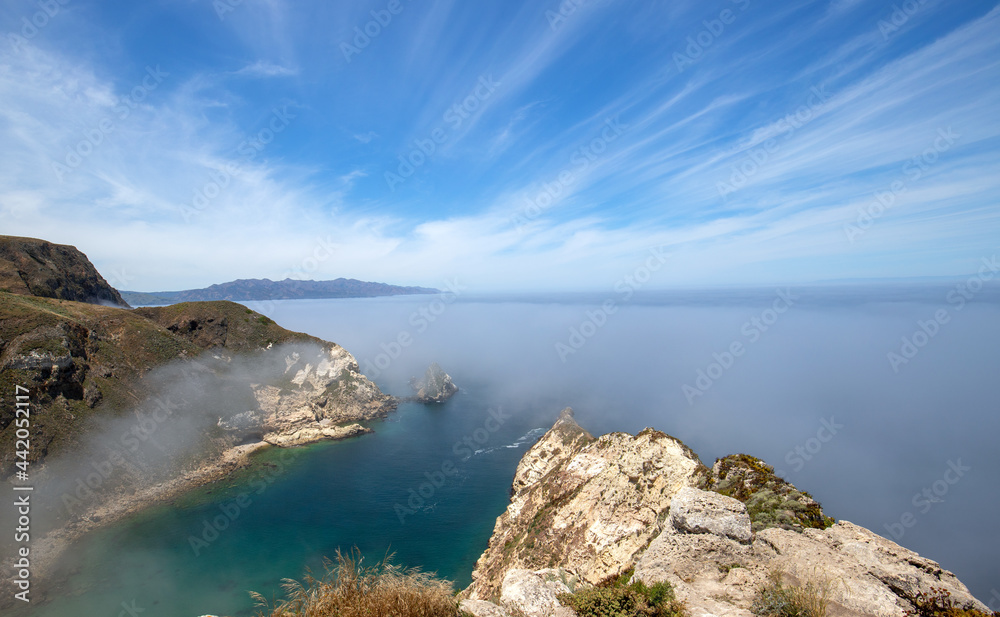 Inversion layer clouds misting over Potato Harbor on Santa Cruz Island with mist coming in under blue cirrus sky in the Channel Islands National Park offshore from Santa Barbara California USA