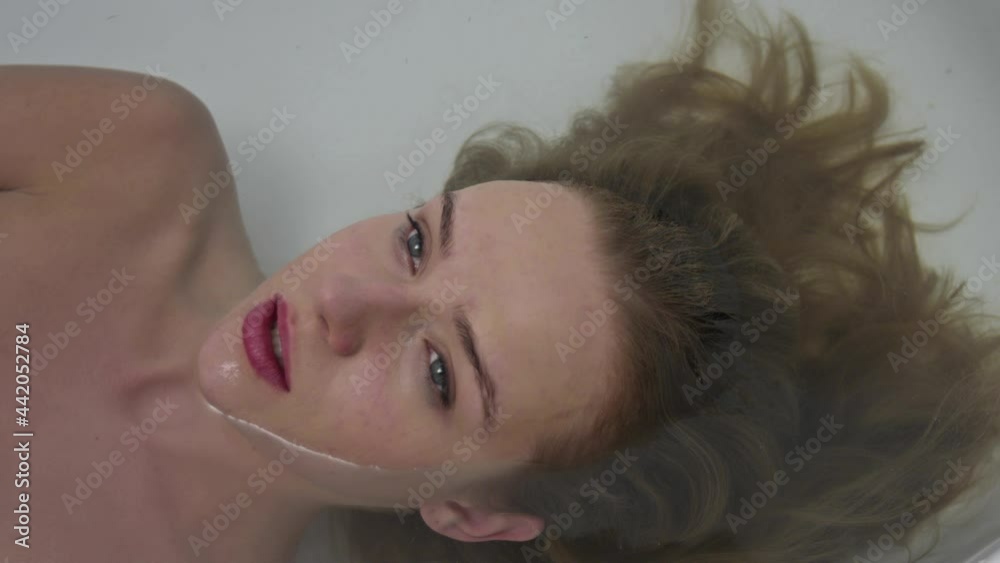 Serious lady with stress laying in the wash tub take a deep breath to drawn in water. Sad woman floating in the bath tub for shower. mysterious thoughts of depression of a woman.