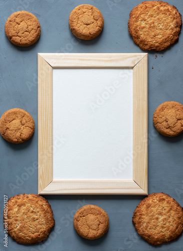 Stationery mock-up scene dedicated to healthy eating. Blank white greeting card in wooden frame surrounded by fresh oatmeal cookies on textured gray background. photo