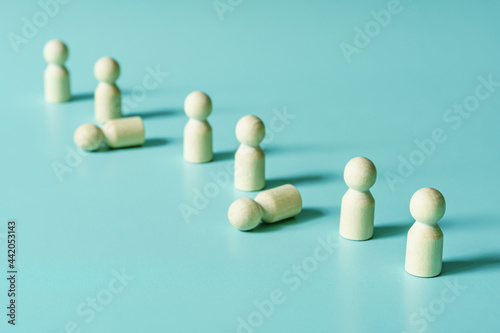 Row line of wooden figures people standing with several fallen. The social concept illustrates that one in three drops out. Blue background with copy space.