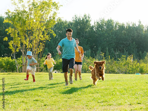 Happy family of four and pet dog playing in the park