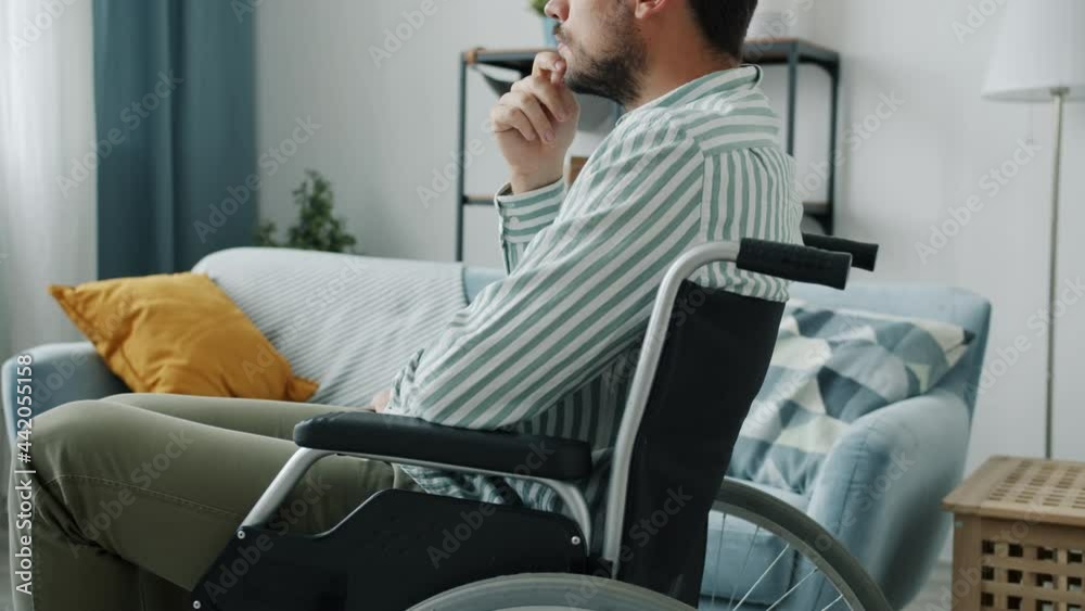 Side view of pensive disabled person in wheelchair thinking indoors in apartment alone. Unhappy handicapped people and leisure time concept. Side view of pensive disabled person in wheelchair thinking indoors in apartment alone. Unhappy handicapped people and leisure time concept.