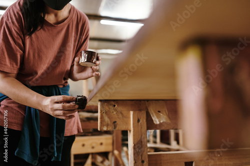 Female carpenter applying protective finish on woodworking project with piece of cloth