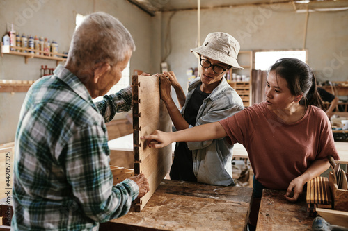 Senior carpenter explaining apprentices how to use butterfly inlay keys when making furniture item © DragonImages