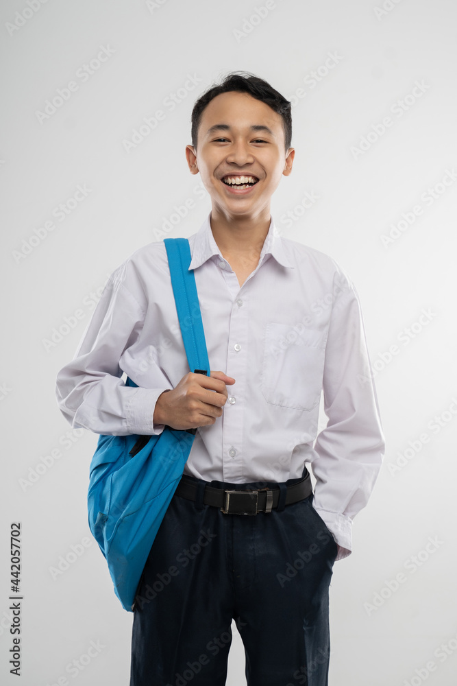a smiling boy wearing a school uniform and carrying a backpack with his hands pocketed in an isolated background a smiling boy wearing a school uniform and carrying a backpack with his hands pocketed in an isolated background