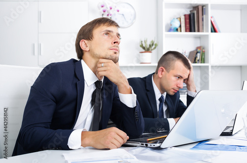 Two sad pensive men coworkers experiencing business failure in firm office