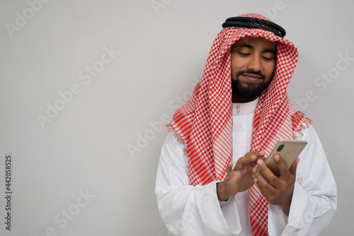 Fotografija an arabian youth in a turban using a mobile phone wiping the screen while smilin