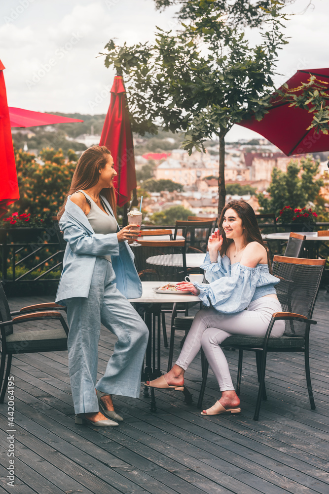Obraz premium two young women friends at a cafe having breakfast, discussing the news, laughing. females in the cafe drink cocktails.