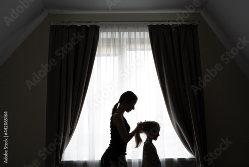 The silhouette of a caring mother combing her daughter's hair