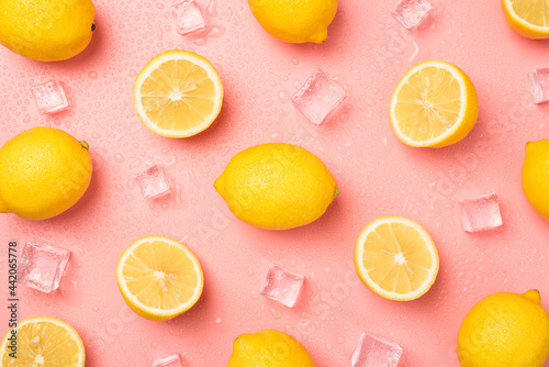 Top view photo of ice cubes water drops halves and whole yellow lemons on isolated pastel pink background