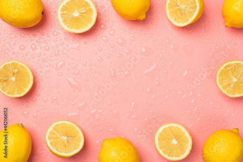 Top view photo of water drops cut and whole yellow juicy lemons on isolated light pink background with copyspace in the middle