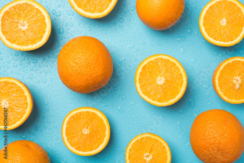 Top view photo of water drops scattered cut and whole oranges on isolated light blue background