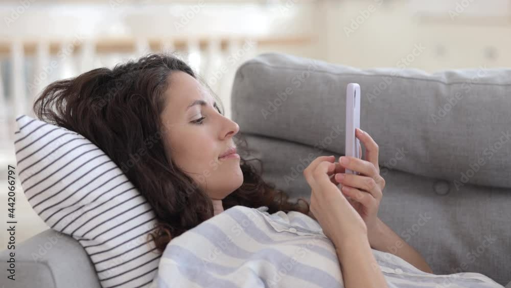 Relaxed millennial woman lying on couch use smartphone message or surfing mobile apps connected to wifi internet. Lazy caucasian female text, send email, shopping online with cellphone gadget at home
