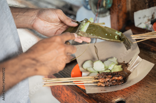 close up of sate ayam preparation served with rice cake or lontong with peanut sauce on food paper photo