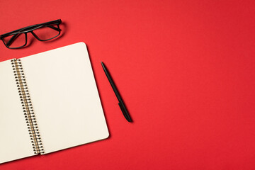 Top view photo of black glasses pen and open spiral notebook on isolated vivid red background with blank space