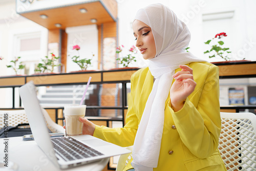 Beautiful young muslim woman using laptop while sitting in cafe