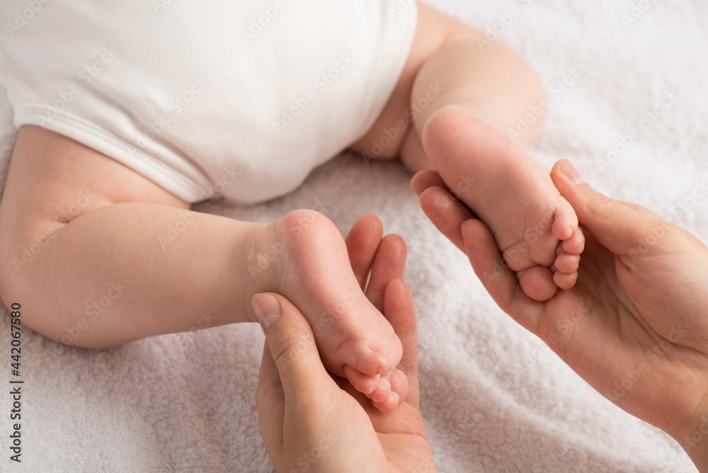 Closeup photo of newborn laying on stomach and mother's hands holding small feet on isolated white cloth background Closeup photo of newborn laying on stomach and mother's hands holding small feet on isolated white cloth background