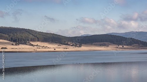 Natural landscape. Beautiful white clouds on blue sky and blurry reflections on the frozen water surface of Batak Dam, lake in the Rhodope Mountains, Bulgaria.