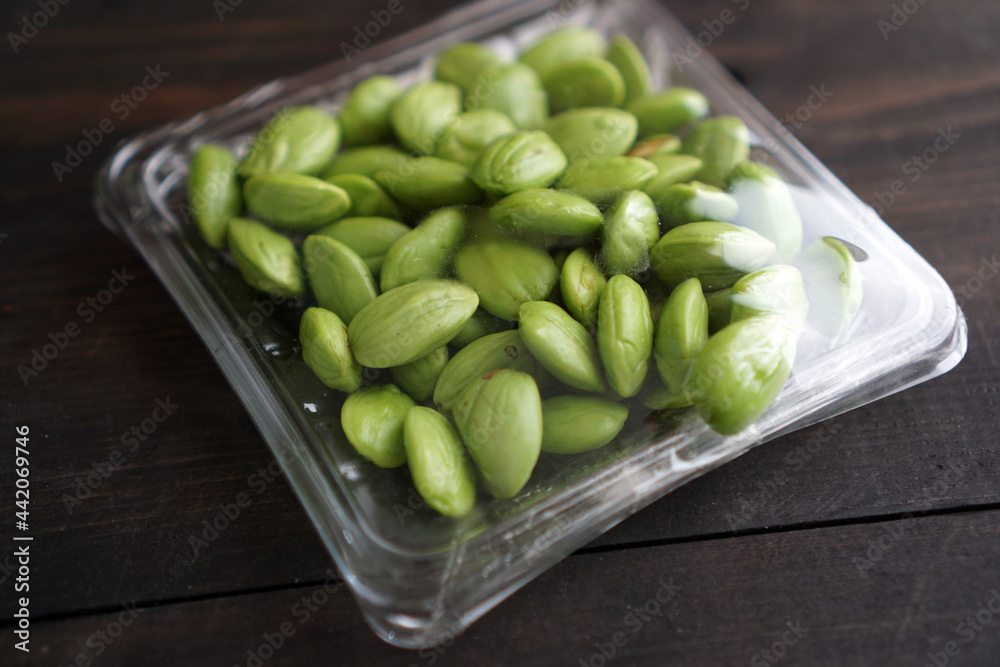 Bitter bean, twisted cluster bean, or stink bean wrapped in plastic on a black wooden table. In Indonesia its called Bitter bean, twisted cluster bean, or stink bean wrapped in plastic on a black wooden table. In Indonesia its called