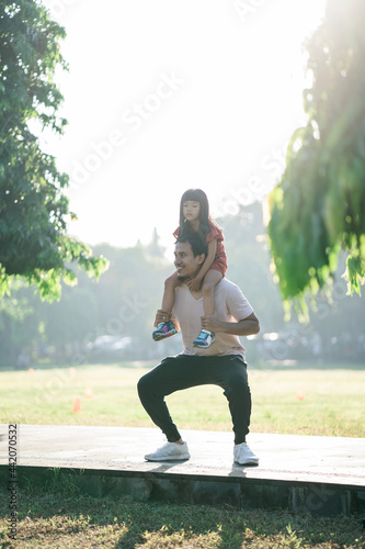 asian father and little daughter do exercises in outdoor. Healthy lifestyle of family with child. dad pushup and child sitting on the back