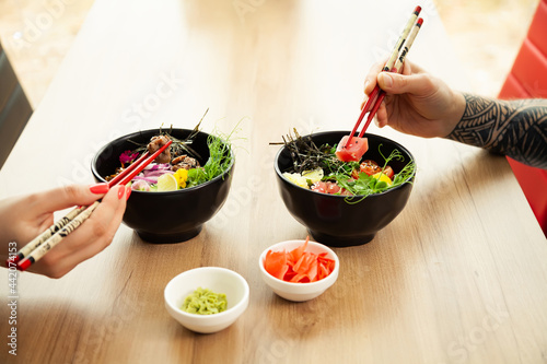 Loving couple man and woman eating salad poke chopsticks. Place the tuna salad in a bowl. People in the restaurant eat salad with chopsticks. Asian seafood salad concept.