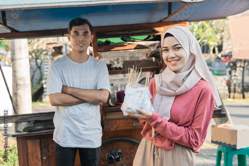 muslim woman ordering chicken satay from small food cart seller. sate ayam street food