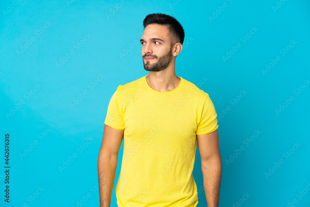 Young caucasian man isolated on blue background having doubts while looking side Young caucasian man isolated on blue background having doubts while looking side