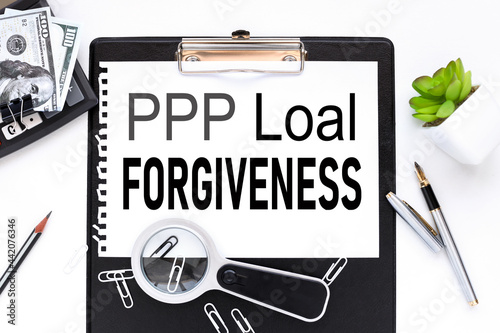 PPP Loan Forgiveness. text on a white sheet of paper near a magnifying glass and a flower in a pot
