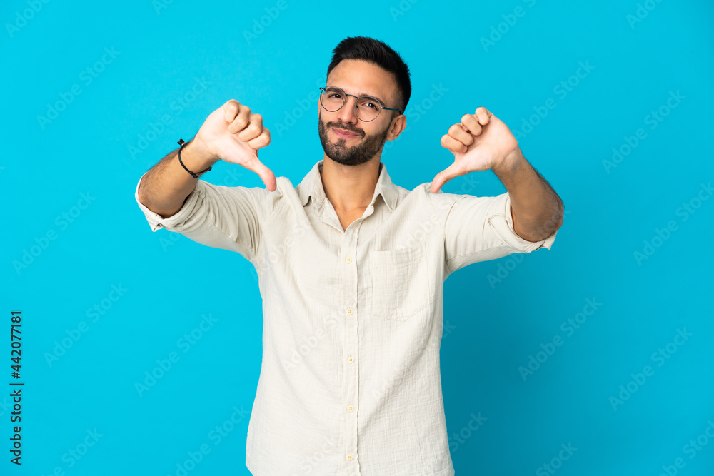 Young caucasian man isolated on blue background showing thumb down with two hands Young caucasian man isolated on blue background showing thumb down with two hands