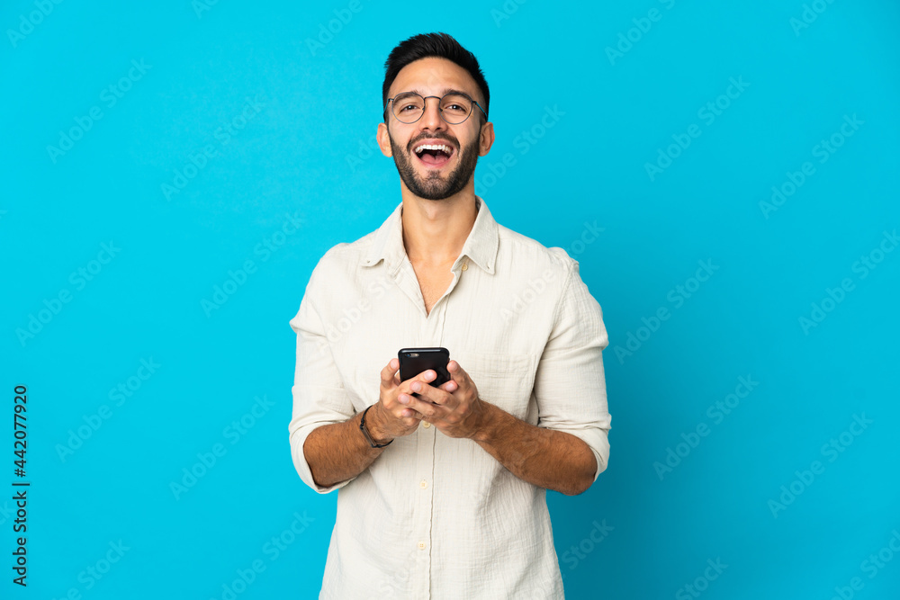 Young caucasian man isolated on blue background surprised and sending a message Young caucasian man isolated on blue background surprised and sending a message
