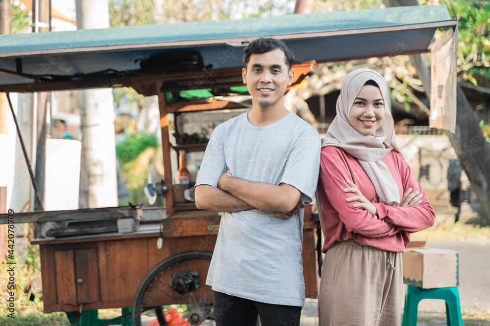 proud couple while selling food on the street. young muslim small business entrepreneur with their food cart at the background