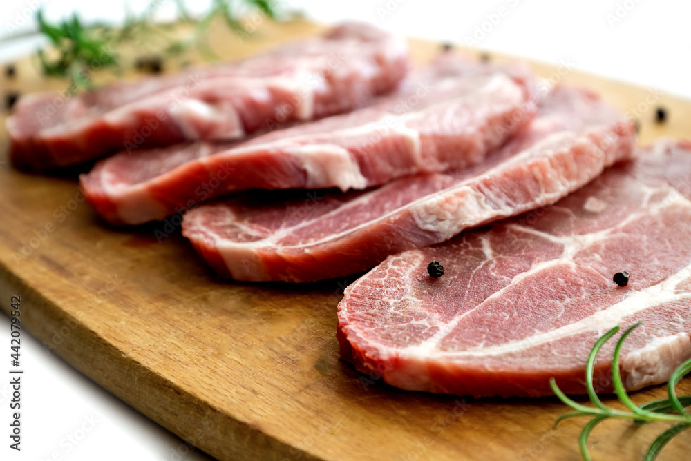 Sliced raw pork meat with fresh rosemary and pepper on cutting board