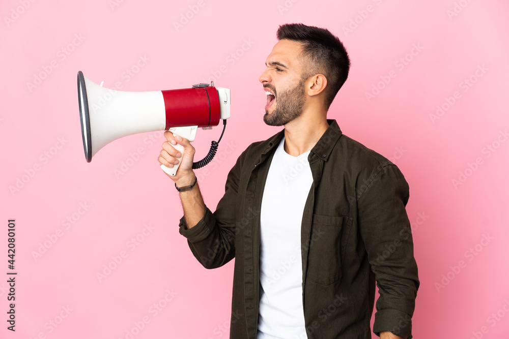 Young caucasian man isolated on pink background shouting through a megaphone to announce something in lateral position Young caucasian man isolated on pink background shouting through a megaphone to announce something in lateral position