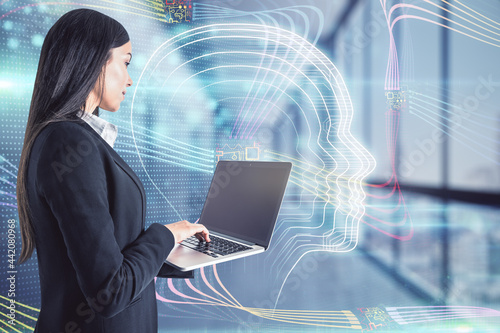 Attractive young european businesswoman with laptop standing in blurry office interior with glowing head hologram. Artificial intelligence concept. Double exposure. photo