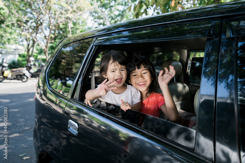 Happy asian siblings waving hands from window and travel by car