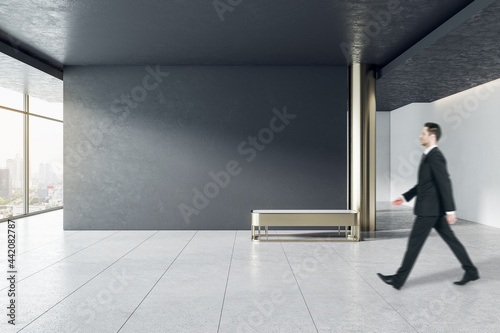 Businessman in modern gallery interior with mock up place on wall and city view.