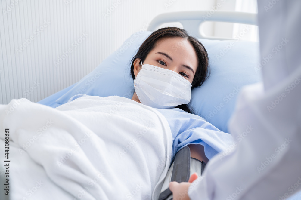 Young woman lying on the hospital bed wearing a mask for checking blood pressure during the outbreak of the coronavirus 19. Concepts to prevent the spread of COVID-19.